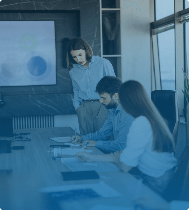 A business meeting in progress with a woman presenting to colleagues while they take notes.