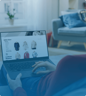 A person browsing an online store on a laptop while relaxing at home, showing an e-commerce website displaying clothing and product categories
