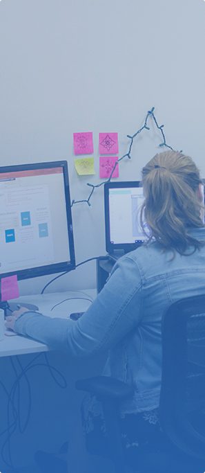 a woman at a workstation with two monitors and post-it note memos