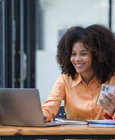 Woman holding a phone seated looking at computer screen