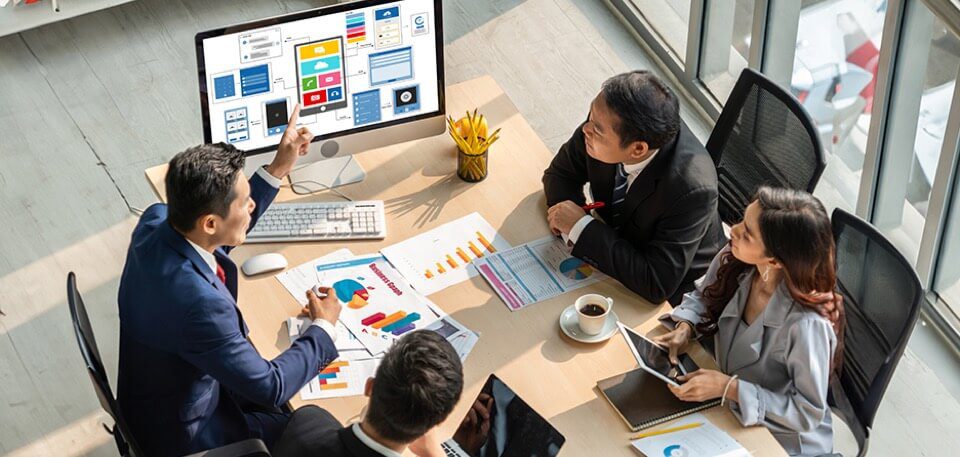 group of office workers gathered around a monitor displaying UI and UX icons