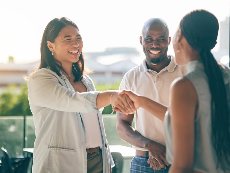 two women shaking hands in front of a man