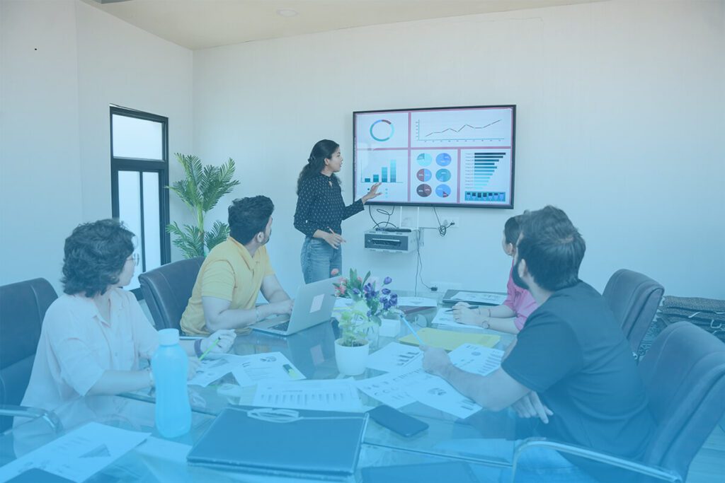 Group of professionals in a meeting room analyzing advertising data displayed on a screen with charts and graphs