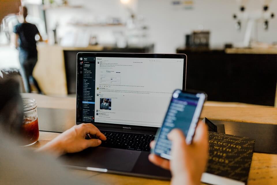 A person holding a phone in one arm and resting the other hand on a laptop’s keyboard.