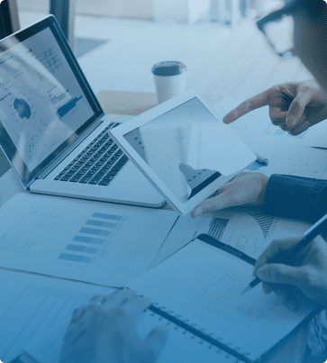 Financial SEO Image: Close-up of hands pointing at a tablet screen with financial charts, surrounded by laptops and documents on a workspace.