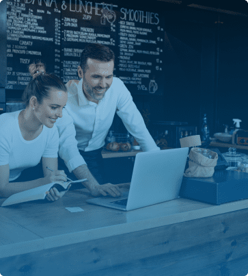 Restaurant SEO Image: A smiling café owner collaborating with a team member, reviewing information on a laptop in a cozy restaurant space.