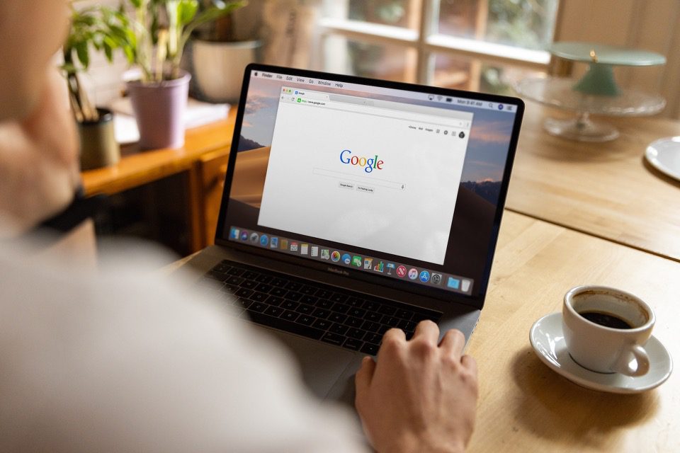 Person Using Google Search on Laptop With Coffee Cup on Table