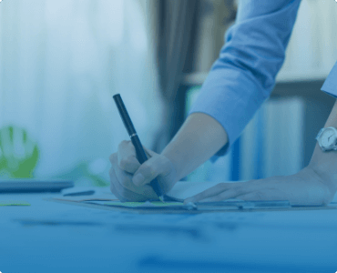 a person writing in a notebook on a cluttered desk
