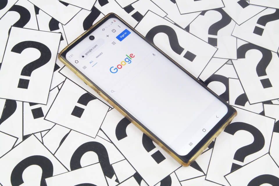 A mobile phone on the Google homepage surrounded by question marks