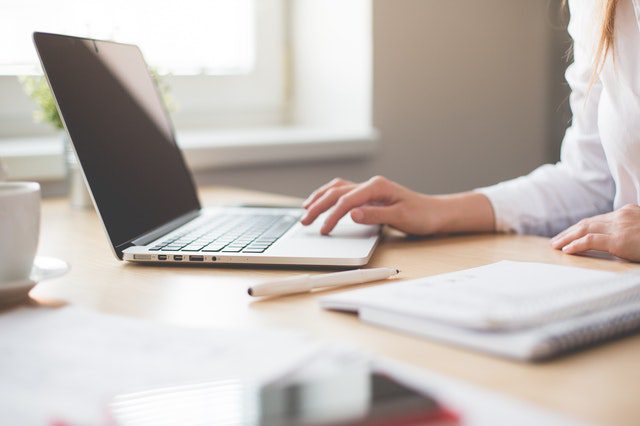 A woman’s hands typing on a laptop in front of a window