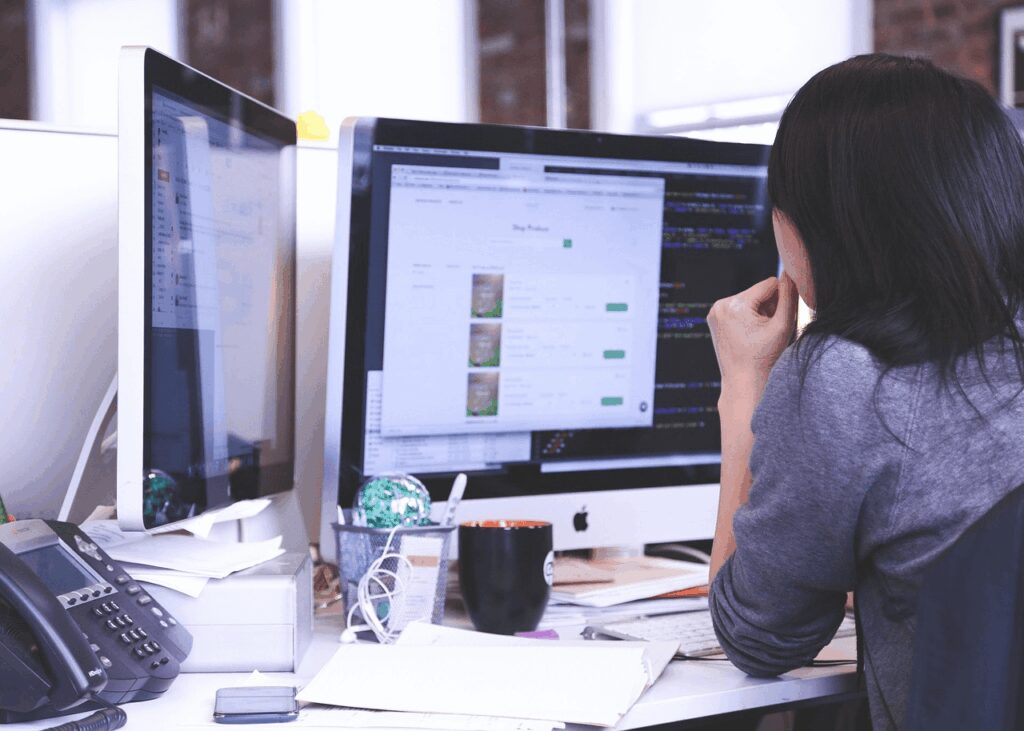 A woman looking at two computer screens